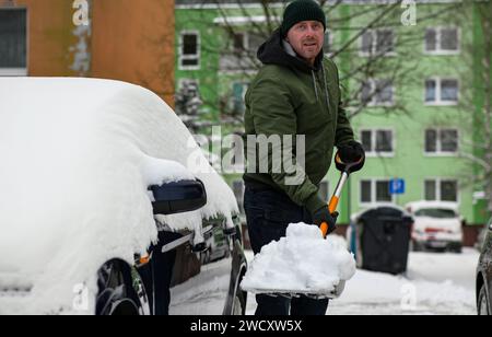 un ragazzo con giacca verde, cappello e guanti usa una pala per lanciare la neve vicino a un'auto dopo una tempesta di neve - vista ravvicinata. Foto Stock