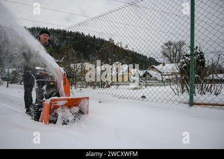 l'uomo spara la neve con una fresa da neve rossa, spruzza la neve lateralmente - vista ravvicinata. Foto Stock