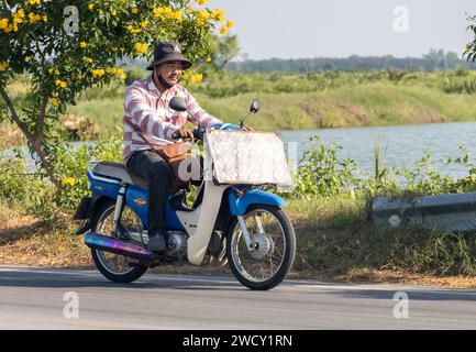 SAMUT PRAKAN, THAILANDIA, 15 dicembre 2023, Un venditore della lotteria cavalca una moto nella campagna tailandese Foto Stock