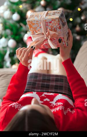 Ragazza in maglione rosso con un regalo sullo sfondo dell'albero di Natale Foto Stock