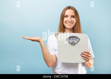 Donna sorridente che presenta una bilancia per il bagno Foto Stock