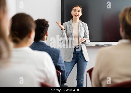 Una coach femminile qualificata e positiva che spiega l'argomento a un gruppo di persone durante una lezione di lingua straniera nell'auditorio Foto Stock