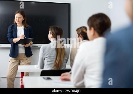 Donna di successo positiva vicino al Consiglio interattivo che conduce corsi di formazione aziendale per il pubblico in classe Foto Stock