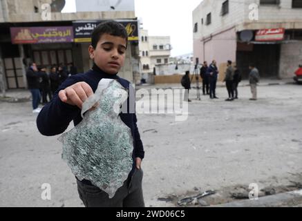 Nablus. 17 gennaio 2024. Un ragazzo raccoglie i detriti di un veicolo bombardato dall'esercito israeliano nella città di Nablus, in Cisgiordania, il 17 gennaio 2024. Almeno sette palestinesi sono stati uccisi mercoledì dagli scioperi israeliani in Cisgiordania, hanno detto fonti mediche e di sicurezza palestinesi. La Palestine Red Crescent Society (PRCS) ha riferito all'inizio di mercoledì che l'esercito israeliano ha bombardato un veicolo palestinese nella città di Nablus nella Cisgiordania settentrionale, portando alla morte di tre palestinesi, tra cui due fratelli del campo profughi di Balata a Nablus. Credito: Ayman Nobani/Xinhua/Alamy Live News Foto Stock