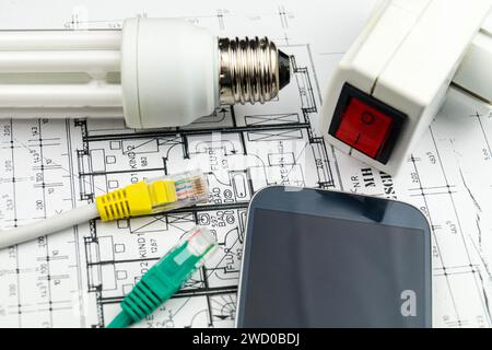 Lampada a risparmio energetico, smartphone e spina di rete sui disegni di costruzione, immagine simbolica per la casa intelligente Foto Stock