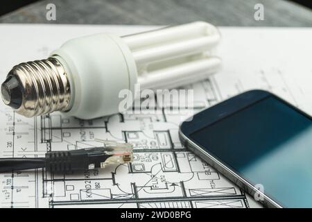 Lampada a risparmio energetico, smartphone e spina di rete sui disegni di costruzione, immagine simbolica per la casa intelligente Foto Stock