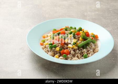 Saporito porridge di orzo perlato con verdure su un tavolo leggermente strutturato, primo piano Foto Stock