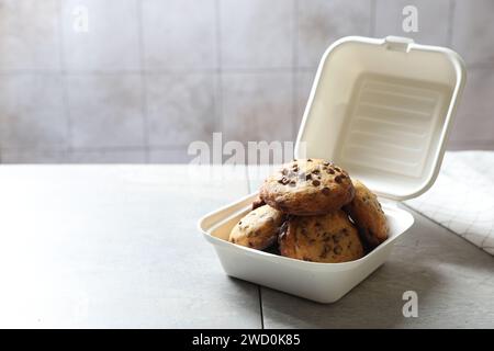 Deliziosi biscotti con gocce di cioccolato in un contenitore di plastica su un tavolo leggero, spazio per il testo Foto Stock