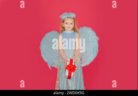 Angelo dei bambini con regalo. Piccolo angelo con ali bianche contiene il regalo. Carino angelo bambina con angeli ali, isolato su rosso. San Valentino Foto Stock