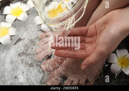 Donna che versa acqua sulla mano mentre immerge i piedi nella ciotola, sopra la vista. Trattamento spa Foto Stock