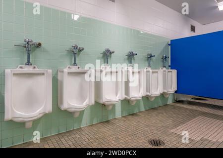 Fila di orinatoi multipli in porcellana bianca in un bagno per uomini più anziani con piastrelle verdi. Foto Stock