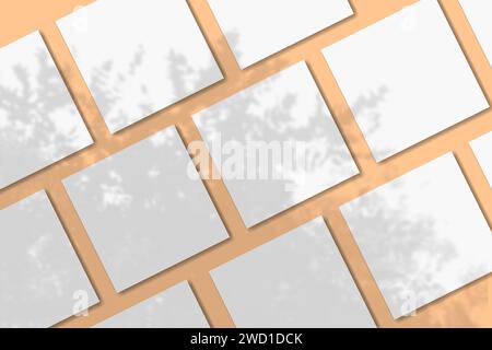 La luce naturale proietta le ombre di un albero tropicale su diversi fogli quadrati di carta ruvida bianca adagiati su uno sfondo arancione. Mockup. Foto Stock