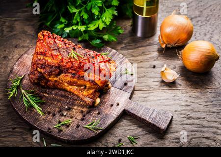 Pancetta di maiale grigliata con buccia croccante, cipolla ed erbe su fondo di legno Foto Stock