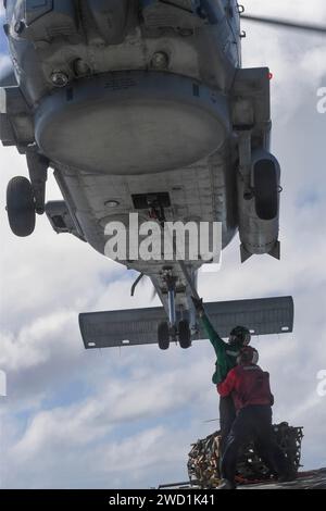 Gli avieri attaccano l'uncino a un elicottero MH-60R Sea Hawk per un rifornimento verticale in mare. Foto Stock