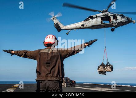 Airman dirige l'equipaggio di un MH-60S Sea Hawk durante un rifornimento verticale in mare. Foto Stock