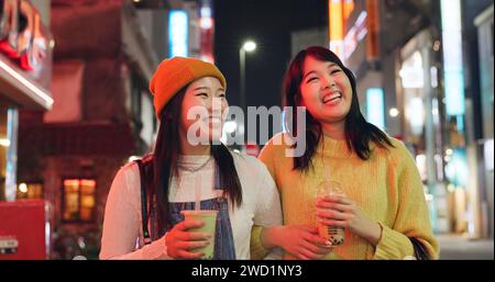 Notte, viaggi e donne giapponesi in una città a piedi, chiacchierando e legando con un drink al frullato all'aperto. Felice, femmina e amica in Giappone con Bubble Foto Stock