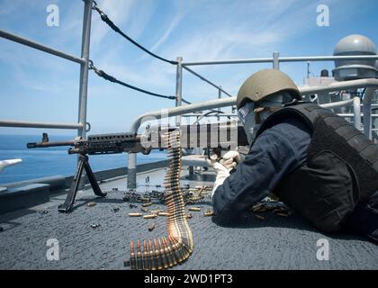 Fire Controlman spara una mitragliatrice M240B sull'ala del ponte di dritta della USS Rushmore. Foto Stock