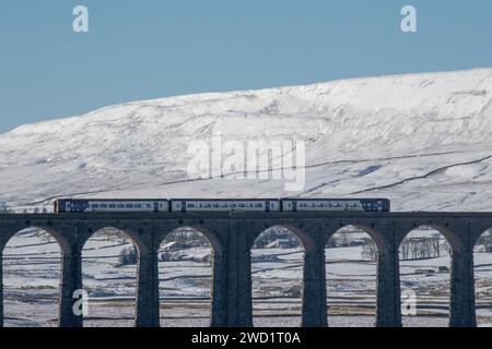 Un treno del nord che attraversa la ferrovia sul viadotto Ribblehead nella neve dello Yorkshire Dales National Park. Preso in una bella giornata di cielo blu. Foto Stock