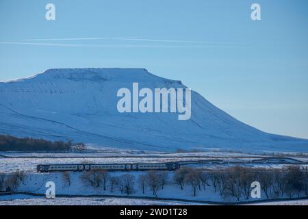 Un treno settentrionale a tre carrozze in una splendida giornata invernale nello Yorkshire Dales National Park, con Ingleborough coperta di neve sullo sfondo. Foto Stock