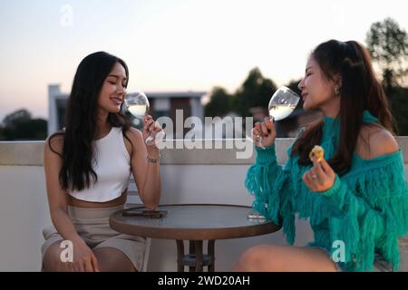 Ritratto di due giovani amiche che parlano e bevono vino sul tetto durante il tramonto Foto Stock