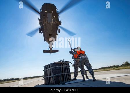 Gli aviatori attaccano una borsa cargo A-22 con 2.000 libbre di provviste di rilievo al gancio di carico di un elicottero UH-60 Black Hawk. Foto Stock