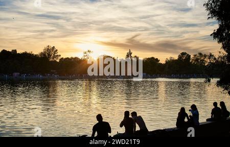 Gente che si rilassa vicino al parco Pond of El Retiro al tramonto nella capitale spagnola. Persone sedute vicino al lago nel Parque de El Retiro. Madrid, Spagna Foto Stock