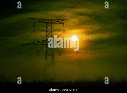 Pilone ad alta tensione al centro della nebbia con il sole dell'alba che lo illumina contro la luce. Francia, Europa Foto Stock