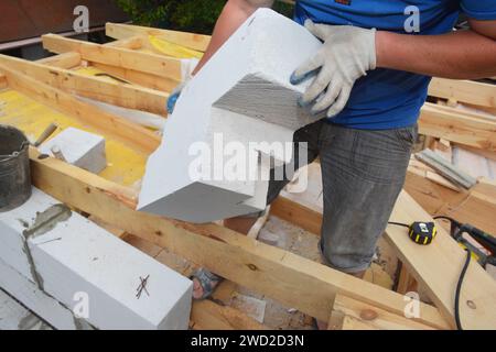 Un imprenditore edile che installa un blocco di calcestruzzo cellulare autoclavato di forma irregolare, tagliato da una sega a mano per posarlo sul bordo di una parete in mattoni del Foto Stock