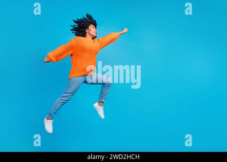 Foto integrale del corpo di una giovane donna attraente che corre per saltare divertiti sbrigati vestiti eleganti in maglia arancione isolati su sfondo di colore blu Foto Stock