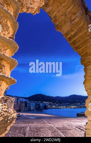 Il pittoresco villaggio di mare di Cefalù visto da un arco di pietra al calar della notte, in Sicilia Foto Stock