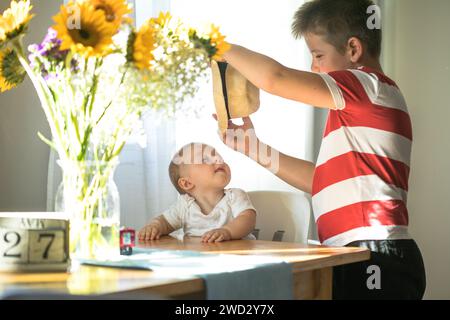 Fratello maggiore che indossa un cappello al fratello minore. Fratelli concettuali e stile di vita sincero Foto Stock