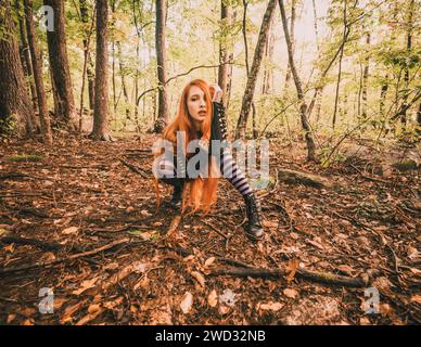 Una giovane donna dai capelli rossi con leggings a righe viola in posa nella foresta Foto Stock