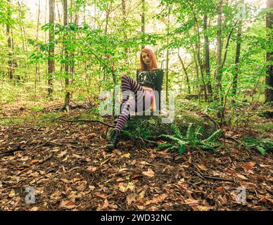 Una giovane donna dai capelli rossi con leggings a righe viola in posa nella foresta verde Foto Stock