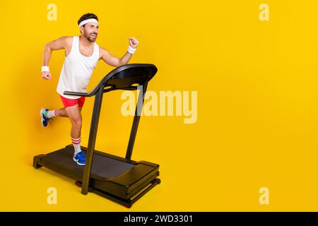 Foto di profilo a grandezza naturale di un bell'uomo goditi lo spazio vuoto del tapis roulant isolato su sfondo giallo Foto Stock