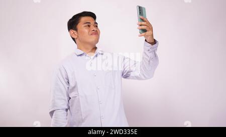 Giovane asiatico effettuare una videochiamata con smartphone su sfondo bianco Foto Stock