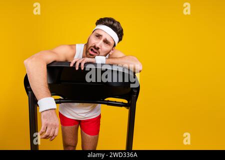 Ritratto di un giovane uomo esausto che lotta per il tapis roulant, spazio vuoto isolato su sfondo giallo Foto Stock