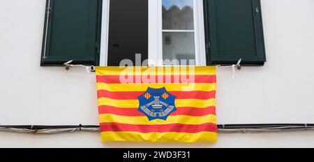 Maó, Minorca, Isole Baleari, Spagna. Colorata bandiera Menorca drappeggiata dalla finestra aperta di una casa della città Vecchia. Foto Stock