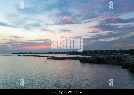 Binibèquer Vell, Minorca, Isole Baleari, Spagna. Vista lungo la costa rocciosa dopo il tramonto, nuvole rosa nel cielo. Foto Stock