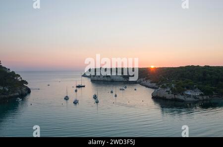 Cala Galdana, Minorca, Isole Baleari, Spagna. Vista sul tranquillo Mar Mediterraneo al tramonto, barche all'ancora. Foto Stock