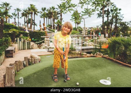 Divertente ragazzo che gioca a mini golf, bambino che ama le vacanze estive Foto Stock
