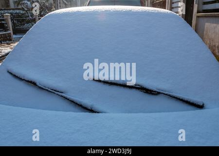 Primo piano del parabrezza di un'auto coperta da uno strato di neve sulla strada in una fredda mattinata invernale Foto Stock