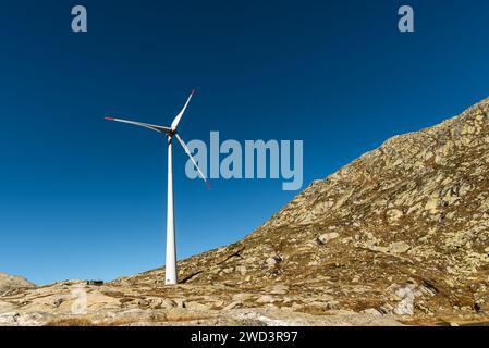 Turbina eolica su rocce contro il cielo azzurro sul passo del San Gottardo, Canton Ticino, Svizzera Foto Stock