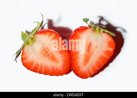 Bacche di fragola tagliate a metà con una foglia su sfondo bianco. Due metà di una bacca. Cibo estivo sano e naturale. Bacca fresca su sfondo bianco Foto Stock