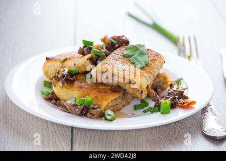 fritti sottili pancake ripieni di carne e funghi, in un piatto su un tavolo di legno chiaro. Foto Stock