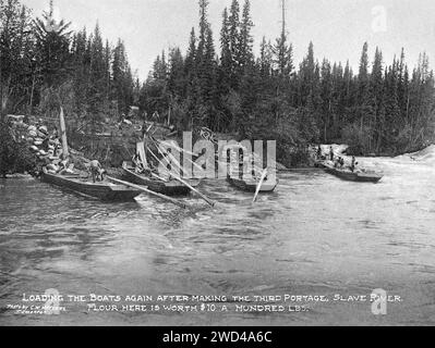 Una fotografia del 1901 di razzi da carico a fondo piatto, caricati dopo essere stati trasportati via terra in un porto sul fiume Slave in Alberta/territori del Nord-Ovest, scattata da C W Mathers in una spedizione nell'estremo nord del Canada e pubblicata nel suo libro «l'estremo Nord». Mathers didascalò questa foto: Caricare di nuovo le barche dopo aver fatto il terzo viaggio, Slave River. La farina qui vale 10 dollari a 100 libbre Foto Stock