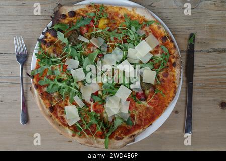 Pizza vegetariana con pezzi di parmigiano e insalata di rucola su un rustico tavolo di legno Foto Stock