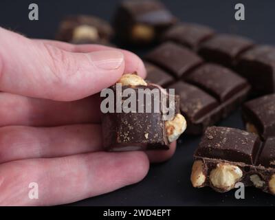 Un uomo che tiene in mano un pezzo di cioccolato fondente con nocciole. Primo piano. Foto Stock