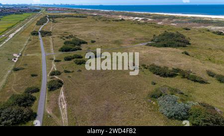 Vista dall'alto del kijkduin della spiaggia e del mare. Sorvola i campi con erba verde ed edifici sulla riva del mare. Tetti di case sullo sfondo. Visualizza da Foto Stock