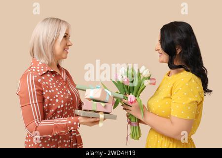 Donne mature con bouquet di splendidi tulipani e confezioni regalo su sfondo beige. Giornata internazionale della donna Foto Stock