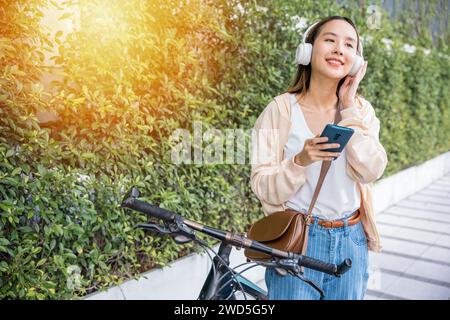 Una donna allegra con la sua bicicletta fa una piacevole passeggiata nel parco in una splendida giornata primaverile. Lei ascolta Foto Stock